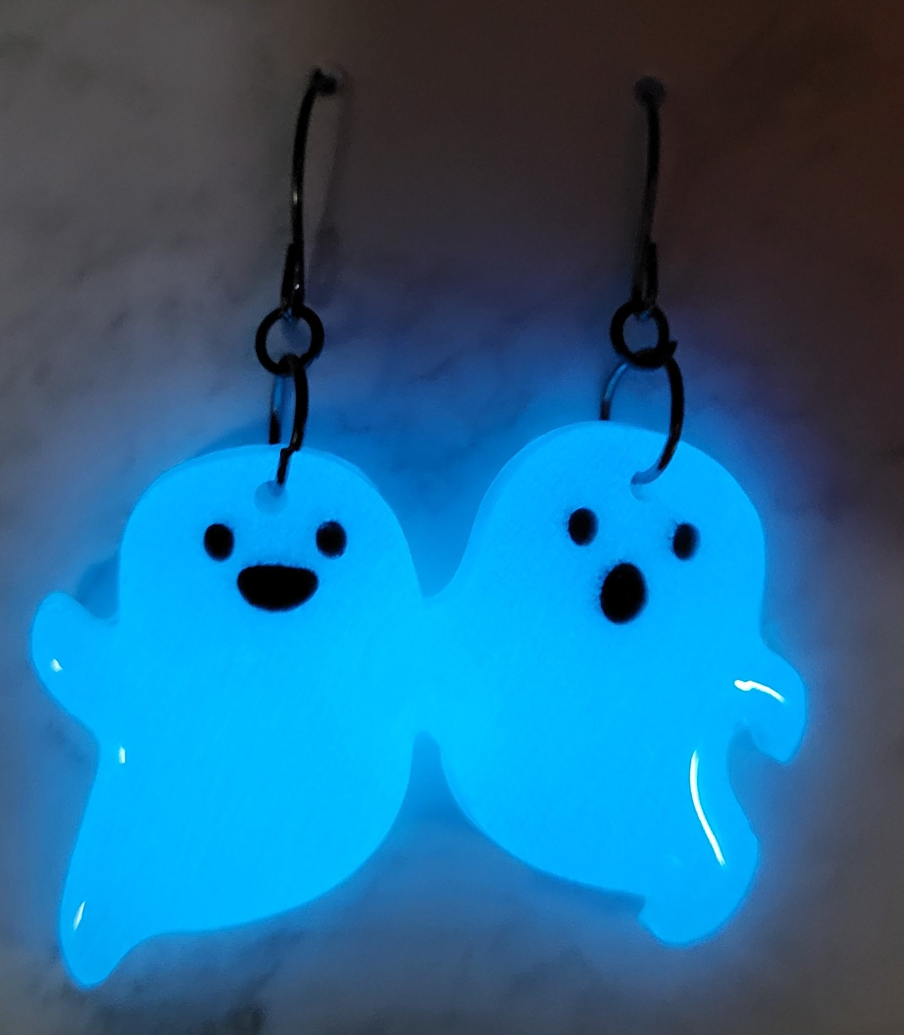 Chunky mismatched ghost resin earrings glowing vivid electric blue in the dark