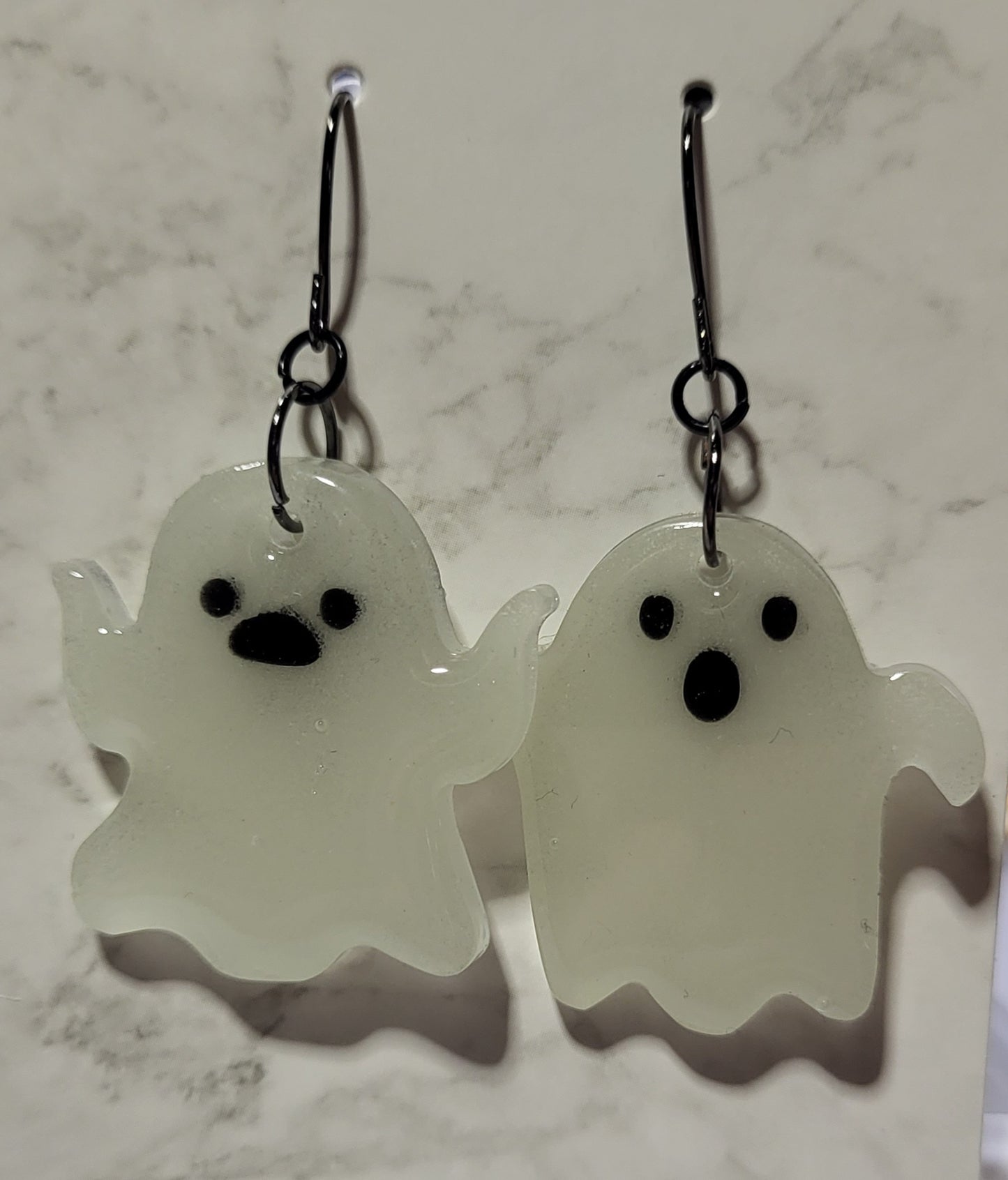 Mismatched waving ghost glow in the dark resin earrings in daylight showing bright white resin on marble surface
