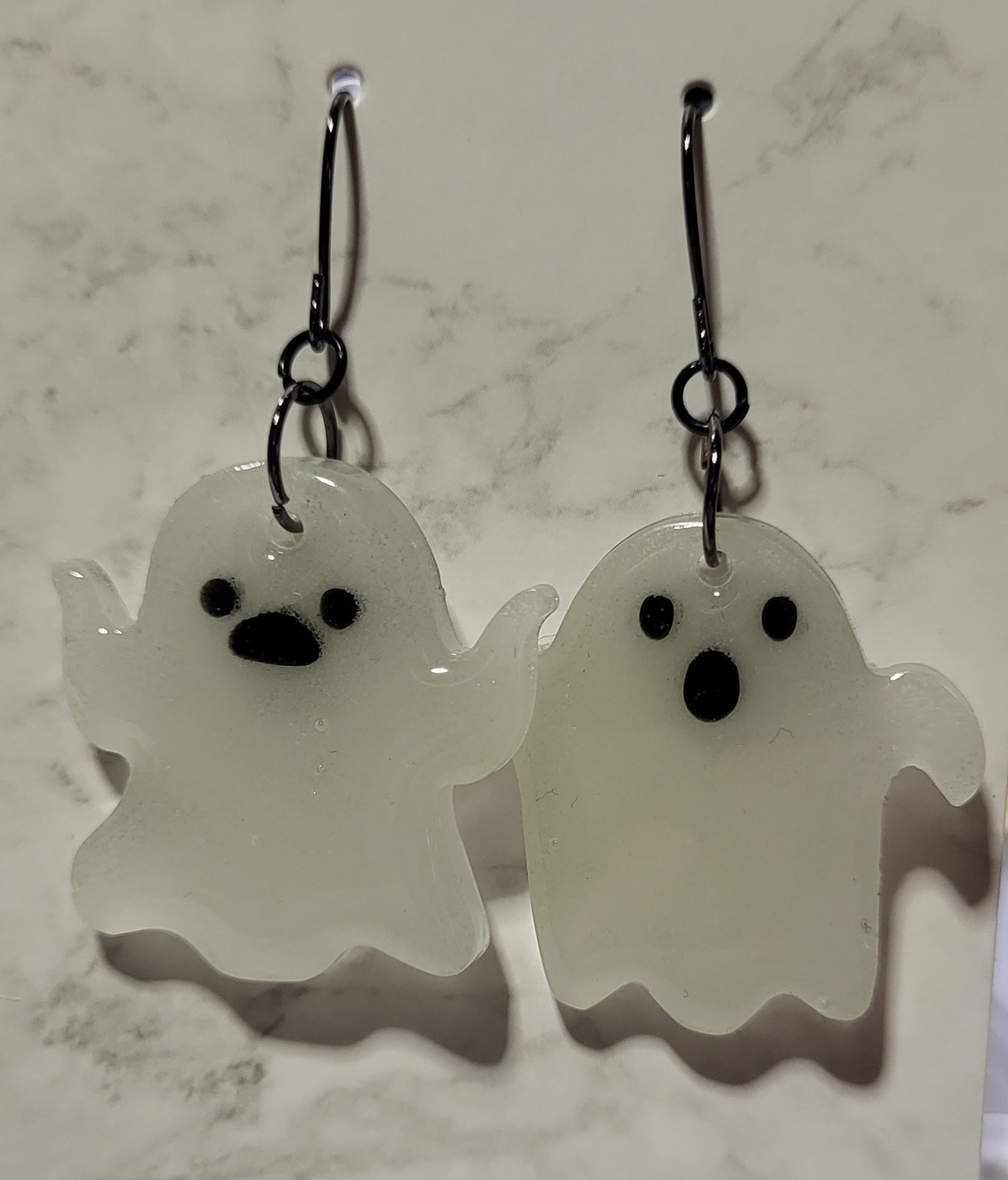 Mismatched waving ghost glow in the dark resin earrings in daylight showing bright white resin on marble surface