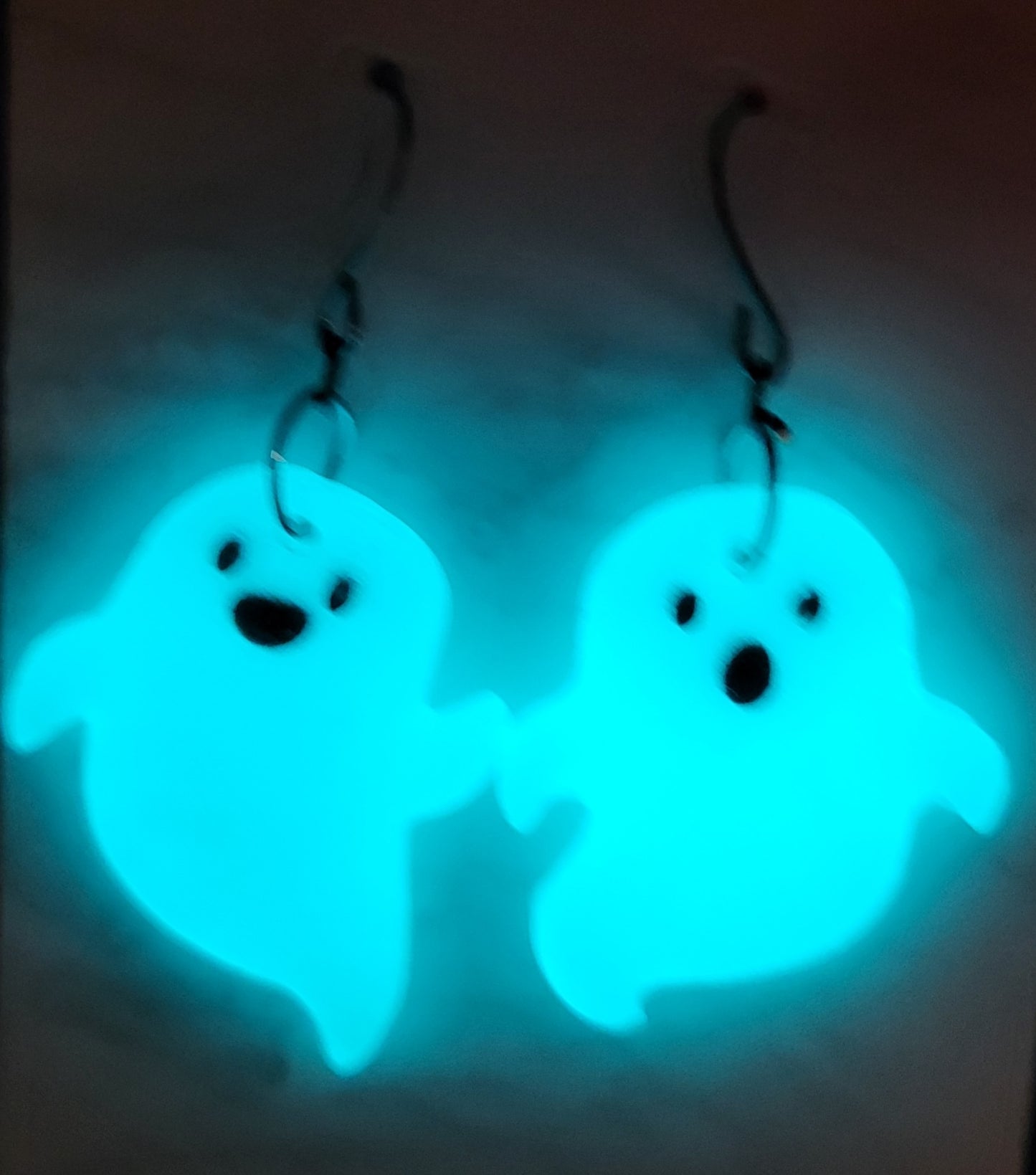 Mismatched ghost resin earrings glowing vivid teal cyan in the dark
