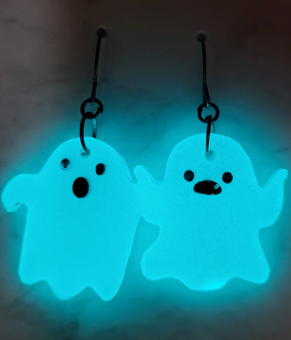 Chunky mismatched ghost resin earrings glowing vivid teal cyan in the dark