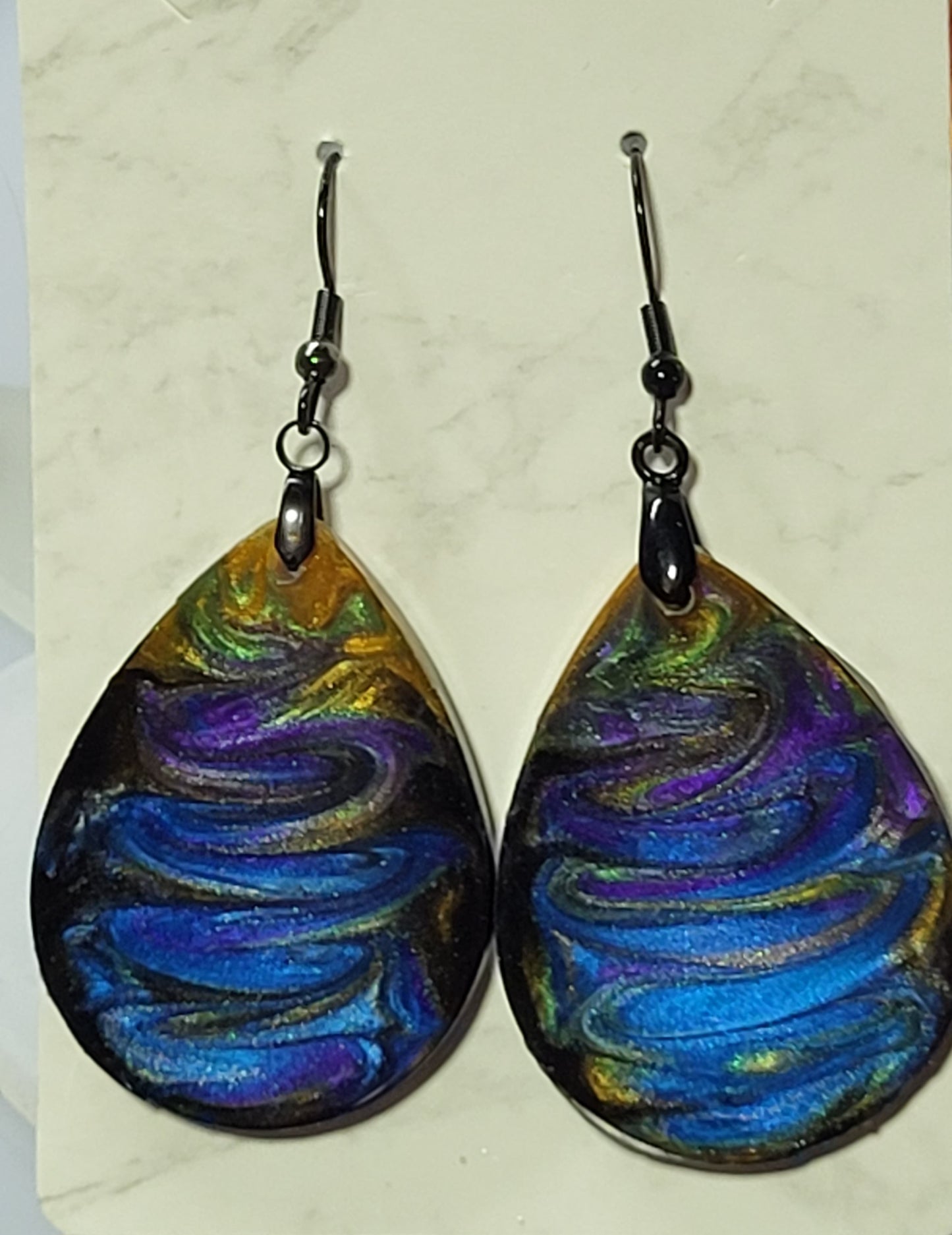 Large teardrop resin earrings with deep galaxy swirl of cobalt blue, purple, and gold with iridescent shimmer on marble surface
