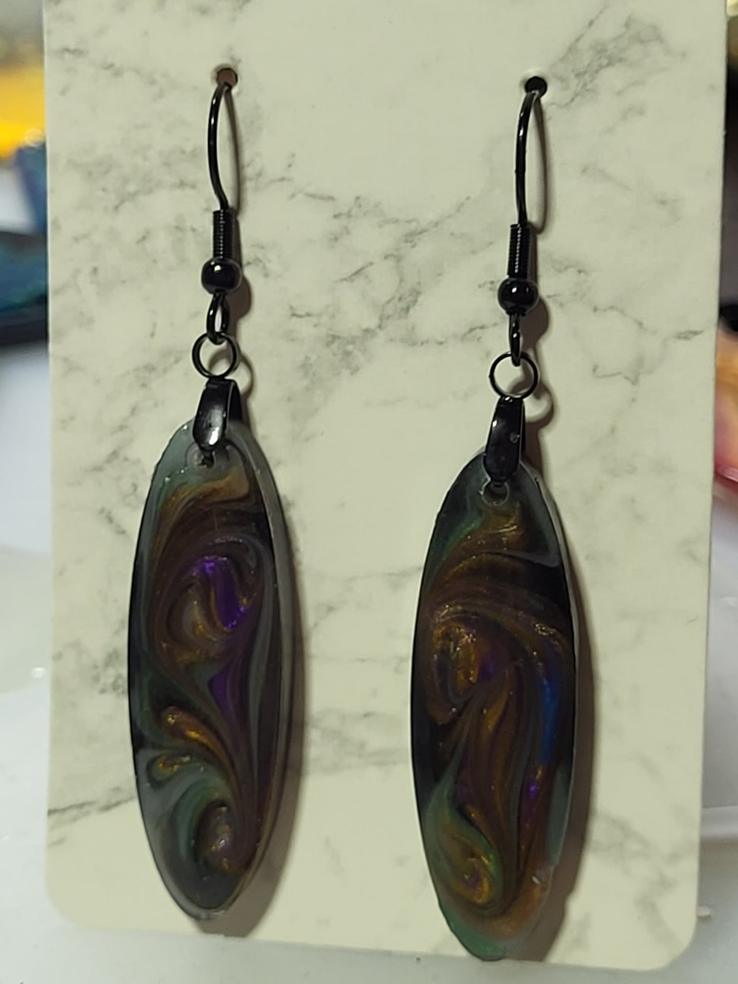 Long slim oval resin earrings with dark galaxy swirl of black, purple, bronze, and teal on marble earring card