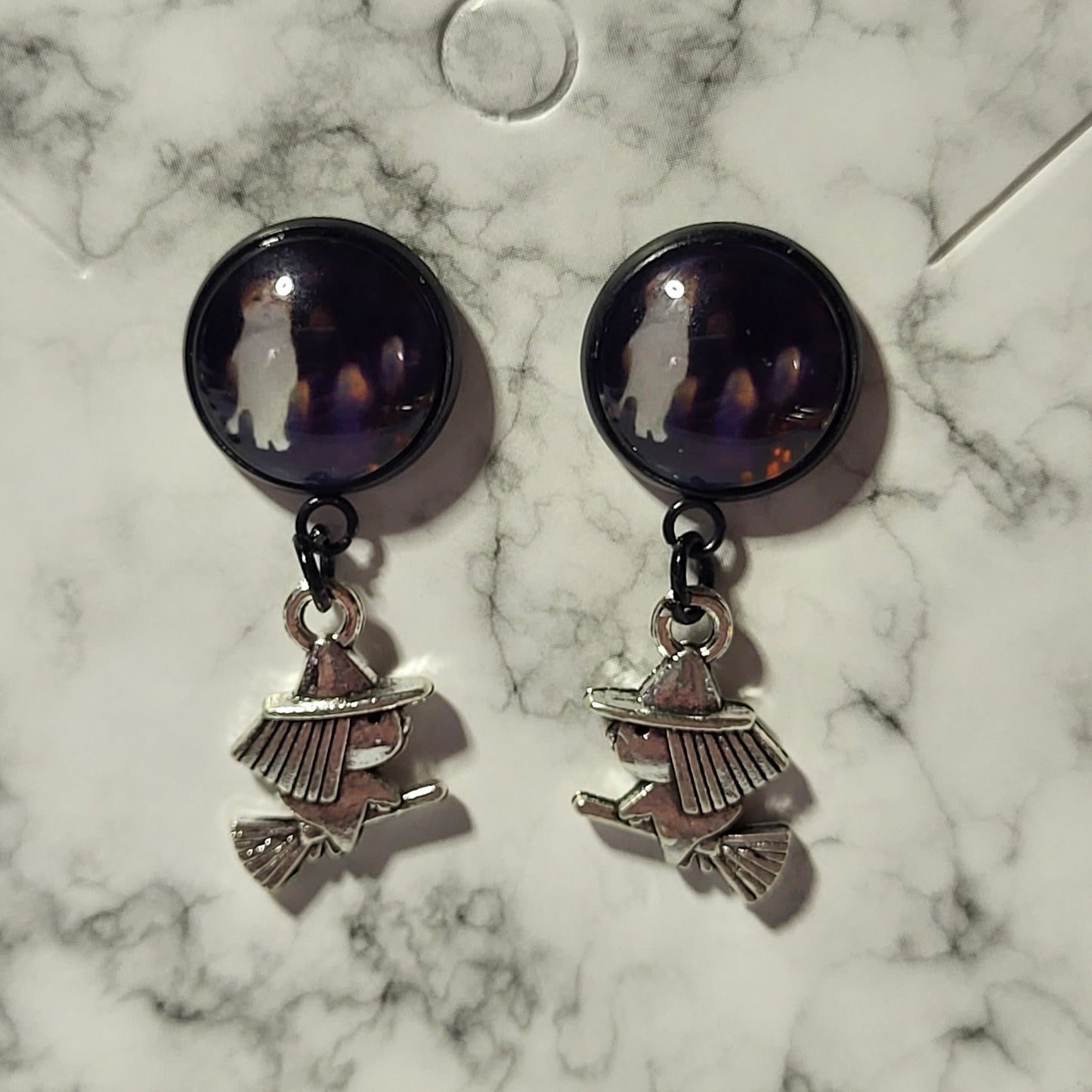 Two-piece drop earrings with deep purple glass dome ghost cab stud top and silver flying witch on broomstick charm on marble earring card