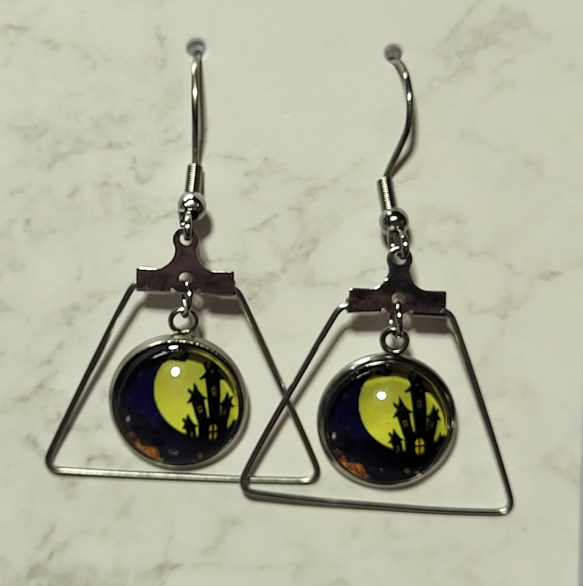 Full moon haunted castle glass dome cab earrings suspended inside open silver trapezoid triangle frame on French wire hook on marble surface
