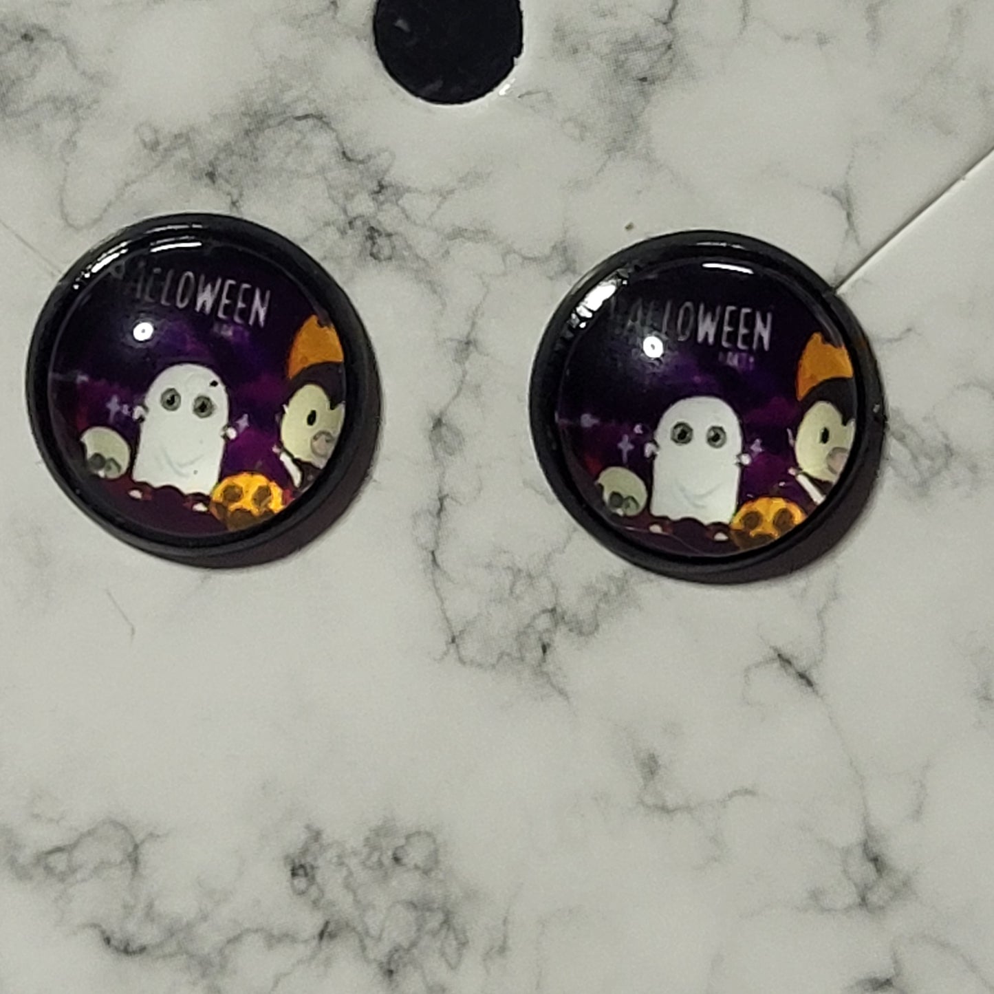 Round glass dome stud earrings in black bezel with kawaii Halloween party scene showing ghost, vampire, and pumpkin on purple background