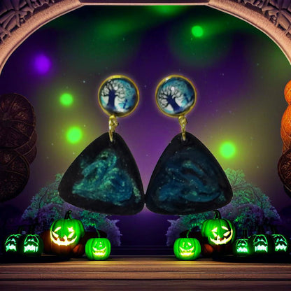 Tree of life cab teal galaxy triangle drop earrings styled against Halloween green pumpkin scene background