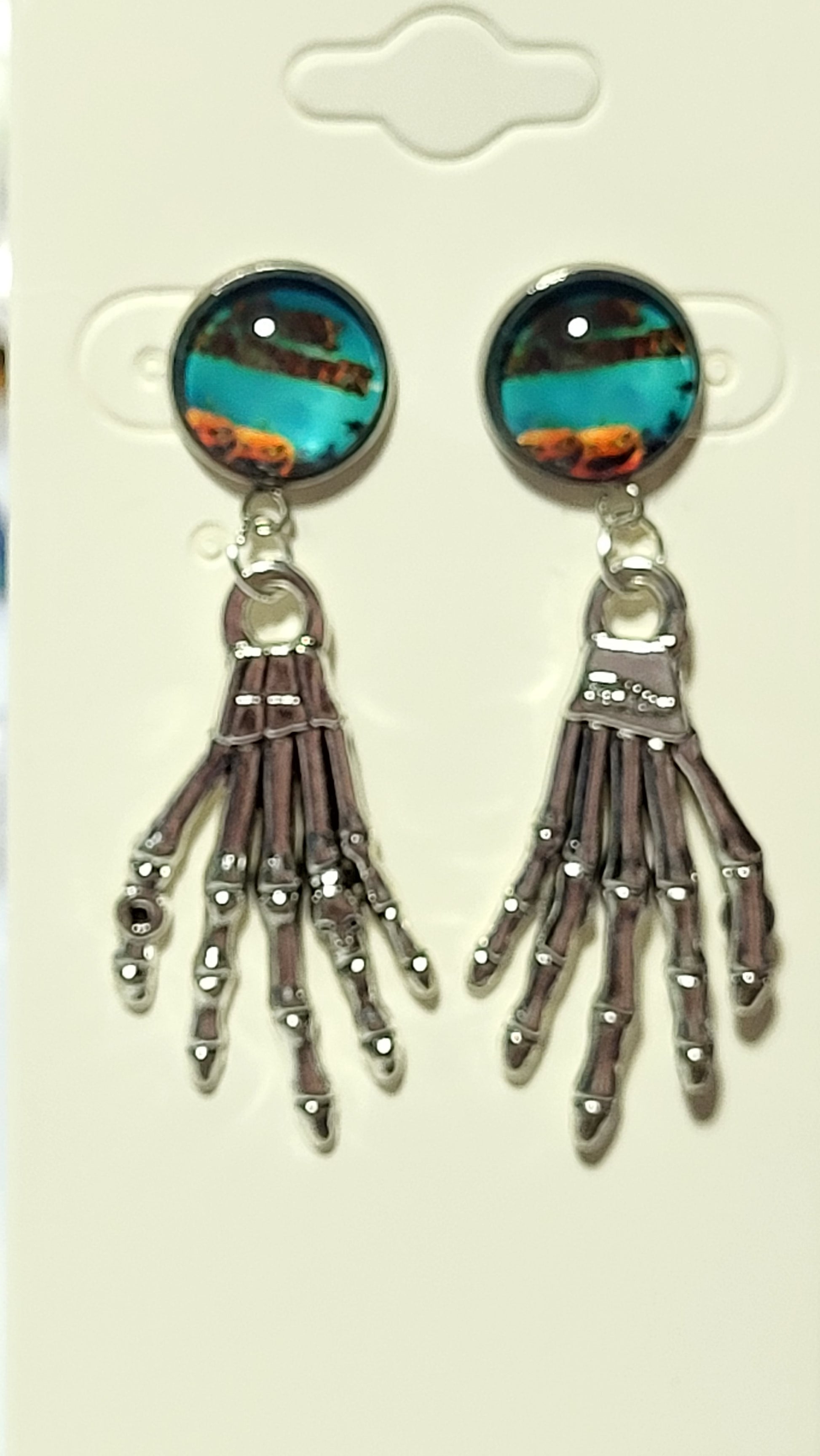 Teal turquoise and amber glass dome cab stud with detailed silver skeleton hand charm on white earring card