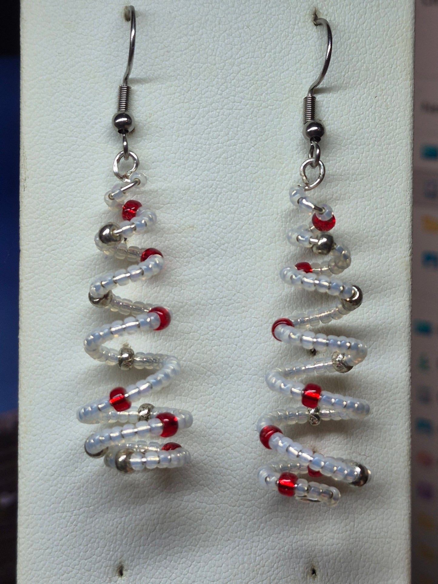Handmade spiral wire Christmas tree earrings with clear white delica seed beads and red silver bead accents on silver French wire on white earring card