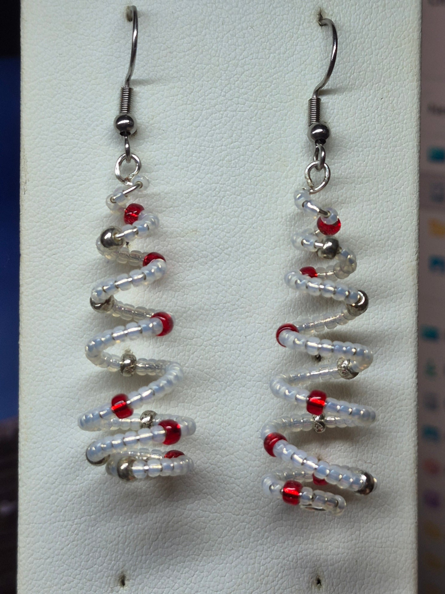 Handmade spiral wire Christmas tree earrings with clear white delica seed beads and red silver bead accents on silver French wire on white earring card