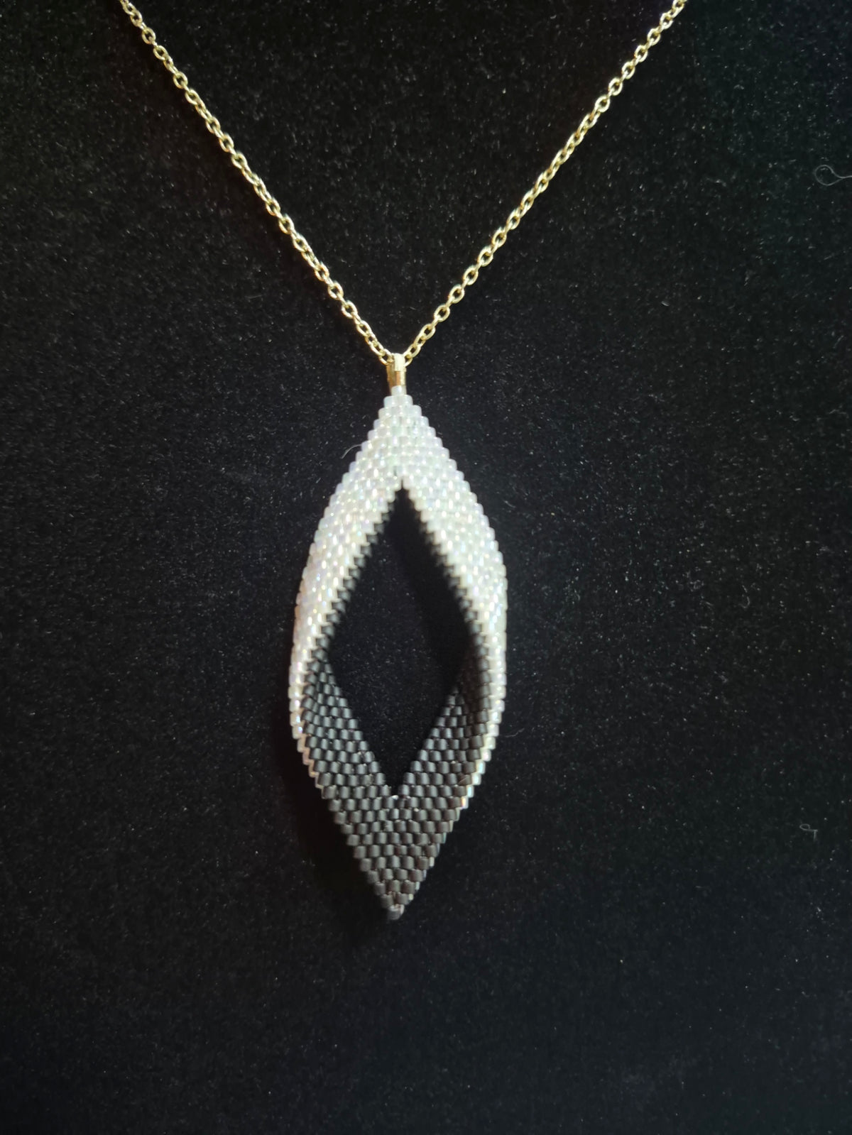 Black and white open leaf beaded pendant on a gold-tone chain against a black background.