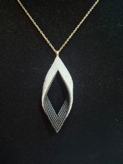 Black and white open leaf beaded pendant on a gold-tone chain against a black background.