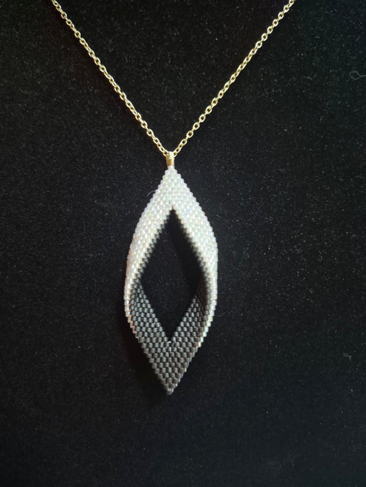 Black and white open leaf beaded pendant on a gold-tone chain against a black background.