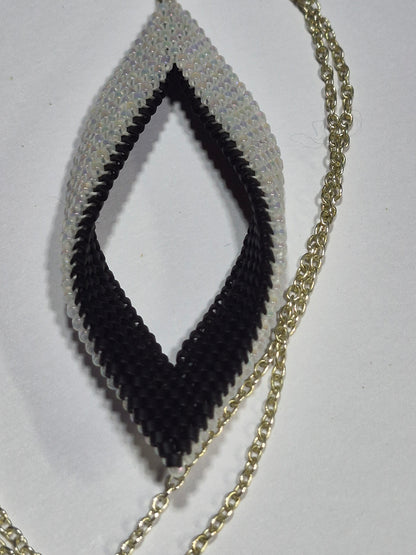 Open leaf pendant with white and black woven beads and a gold-tone chain on a white surface.