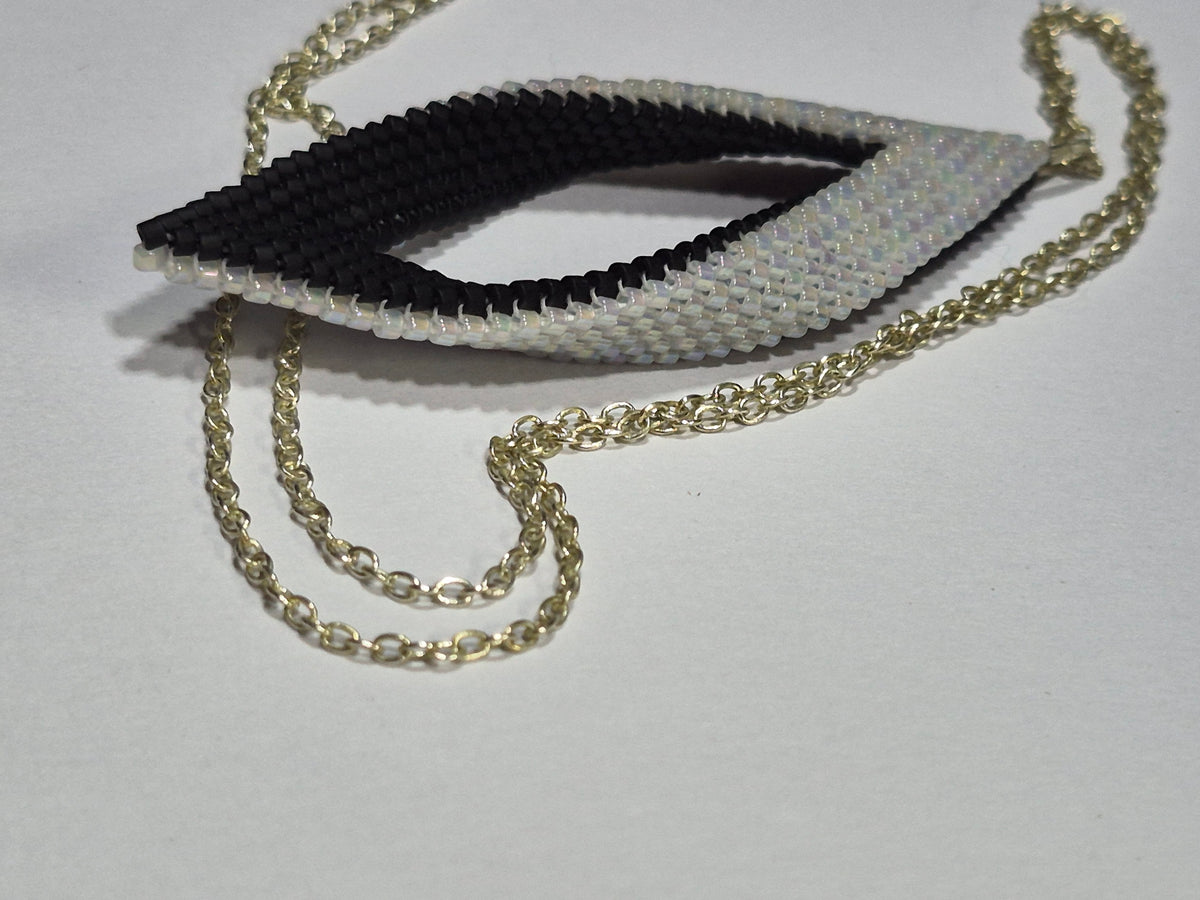 Angled side view of the curved black and white beaded leaf pendant with its gold-tone chain.