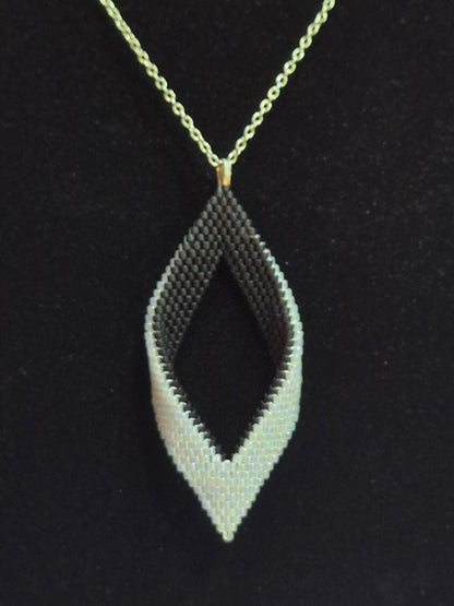 Alternate view of the black and white open leaf pendant hanging from a gold-tone chain.