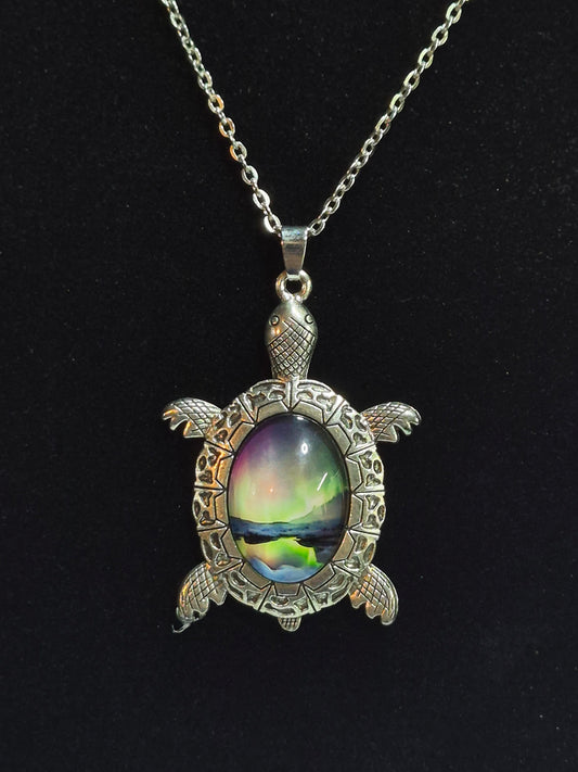 Silver-tone sea turtle pendant with a northern lights landscape cabochon on a black background.