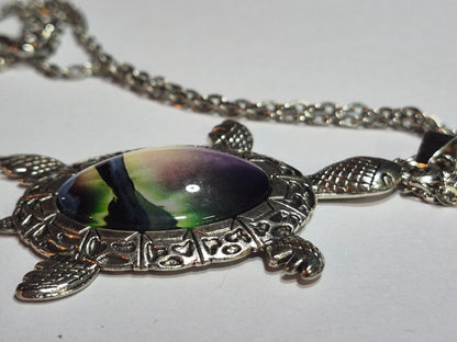 Side view of the domed northern lights cabochon in a detailed silver-tone sea turtle setting.