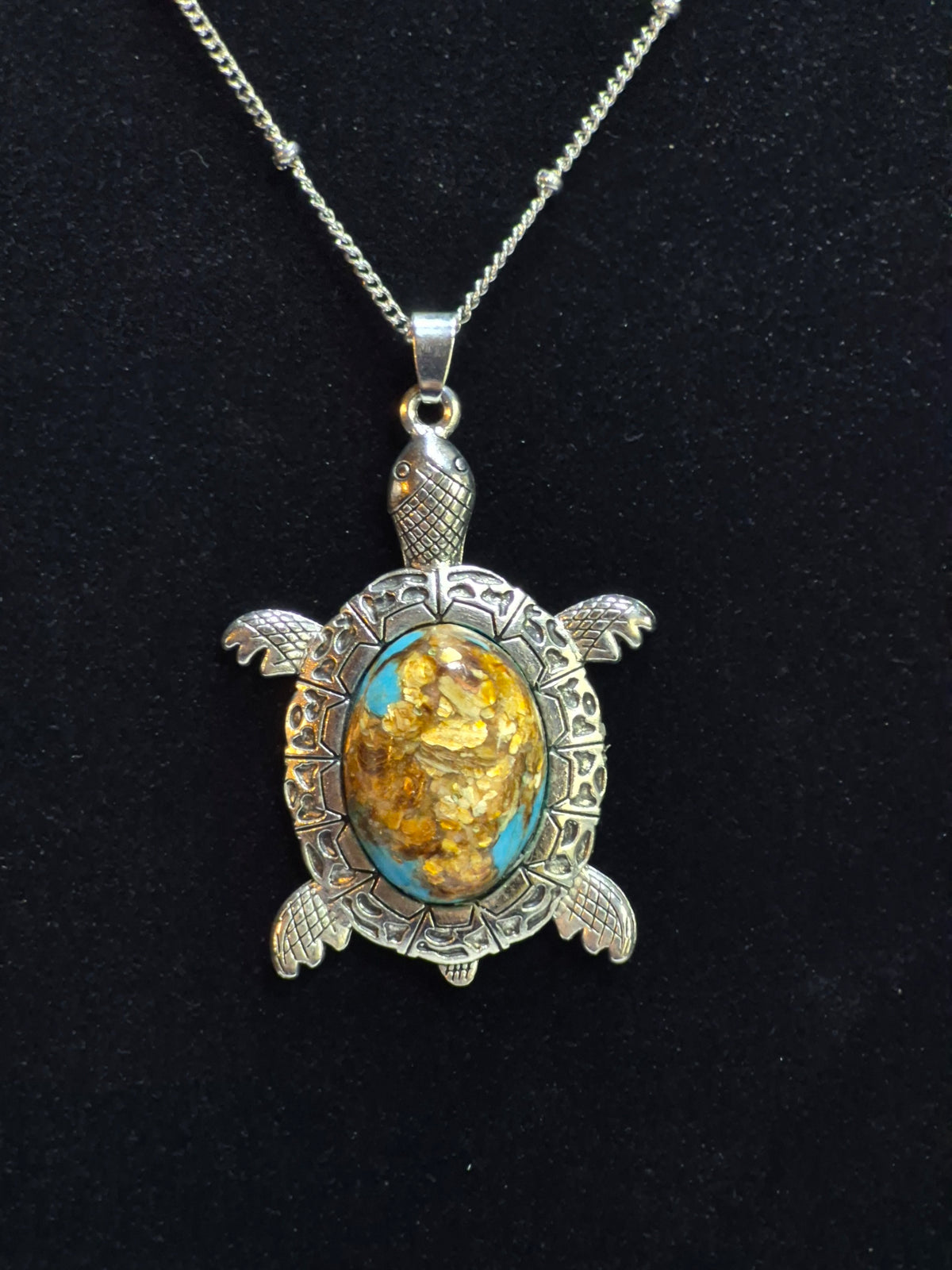Silver-tone sea turtle pendant with a turquoise-blue, brown, and golden-flecked cabochon on black.