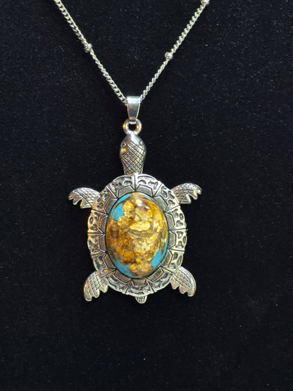 Silver-tone sea turtle pendant with a turquoise-blue, brown, and golden-flecked cabochon on black.