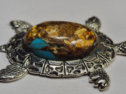 Close-up side view of the turtle's domed brown and turquoise-blue cabochon with golden flecks.