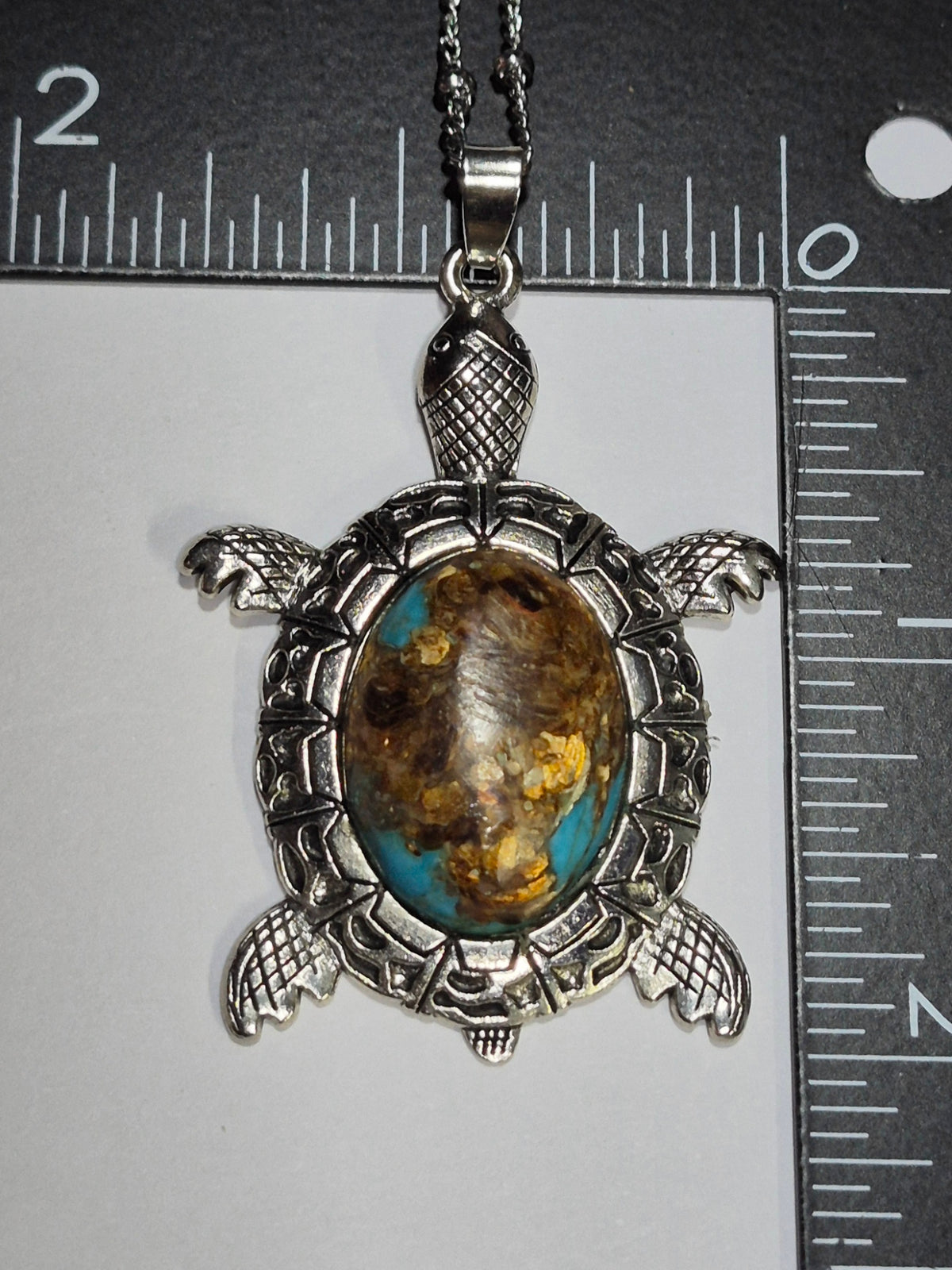Sea turtle cabochon pendant beside rulers showing its size and detailed silver-tone setting.
