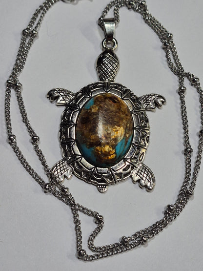 Turquoise-blue and brown sea turtle pendant surrounded by its silver-tone chain on white.