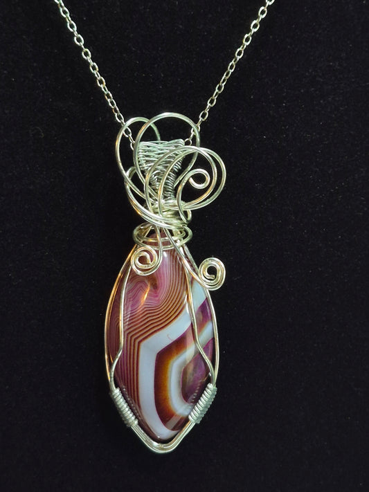 Purple, white, and brown banded oval pendant with silver-tone wire spirals displayed on black.