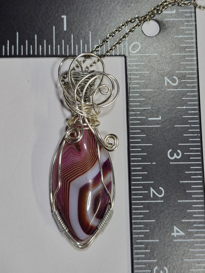 Wire-wrapped purple and white banded pendant beside a ruler for scale.