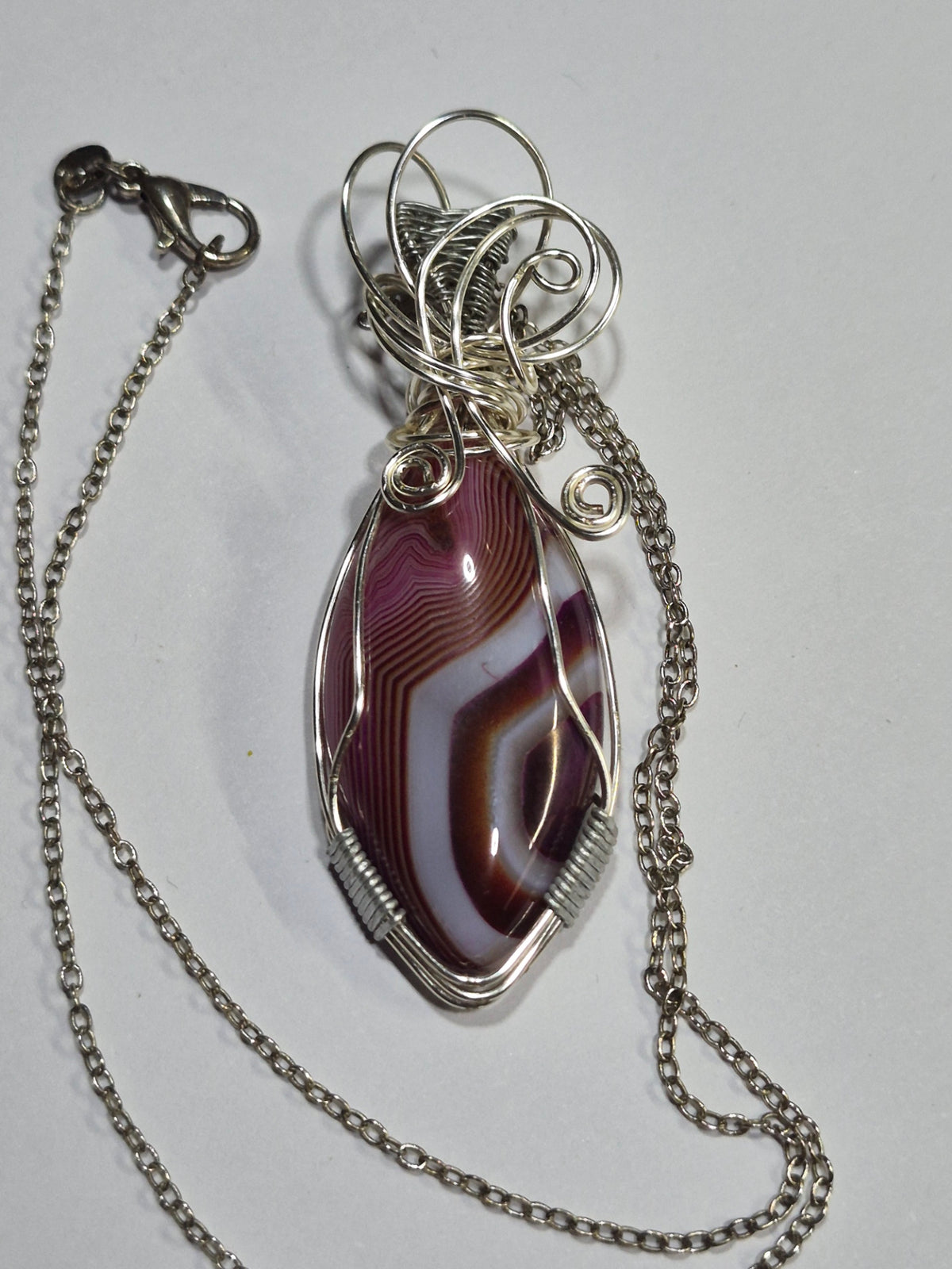 Purple banded pendant necklace with silver-tone copper wirework and chain on a white background.
