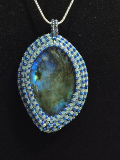Oval blue-flash cabochon pendant with a blue and white beadwoven bezel on a black background.