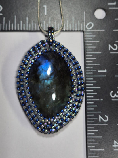Blue and white beadwoven oval pendant beside rulers showing its size.