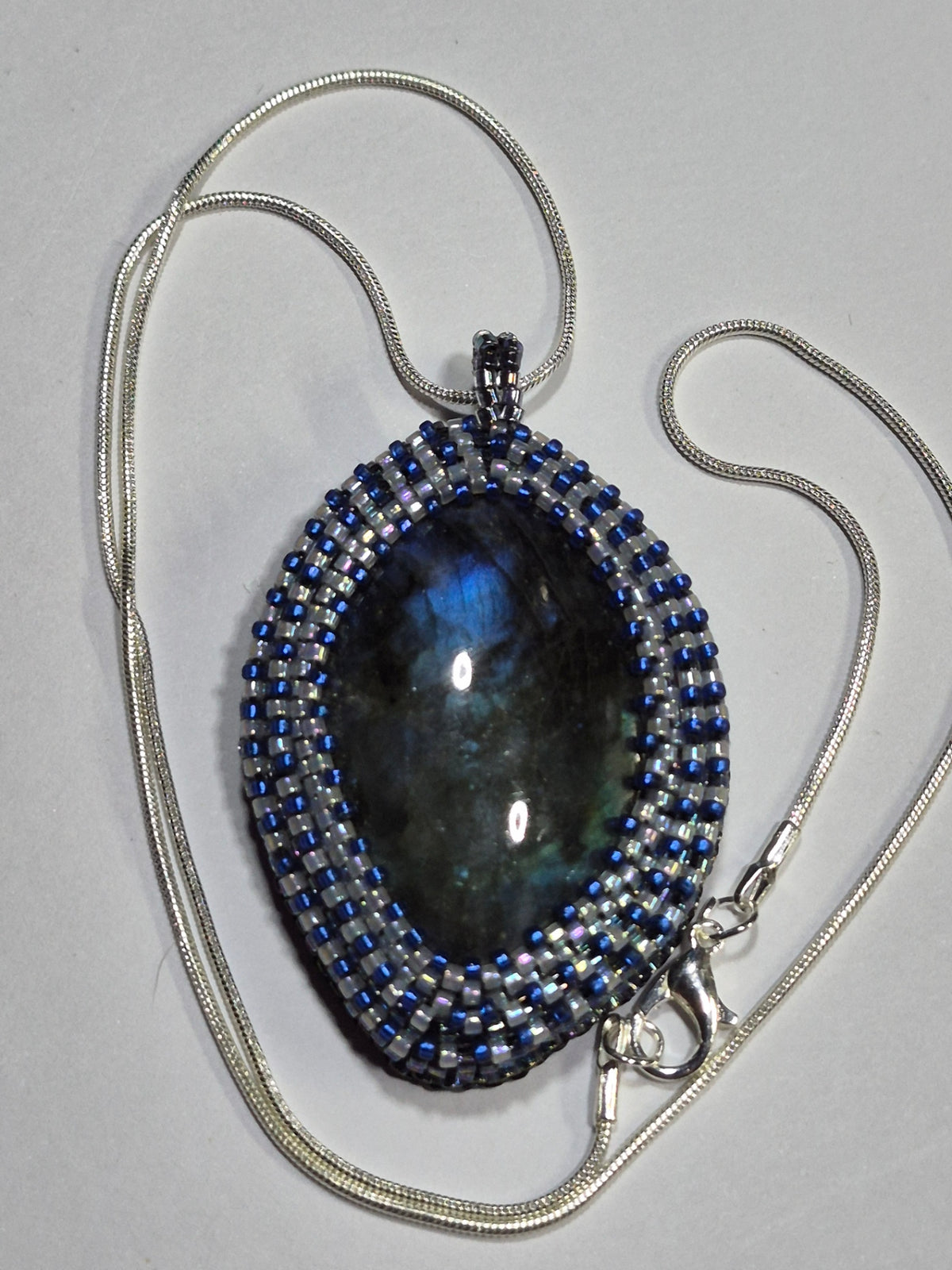 Beadwoven oval cabochon necklace with a silver-tone chain and clasp on a white surface.