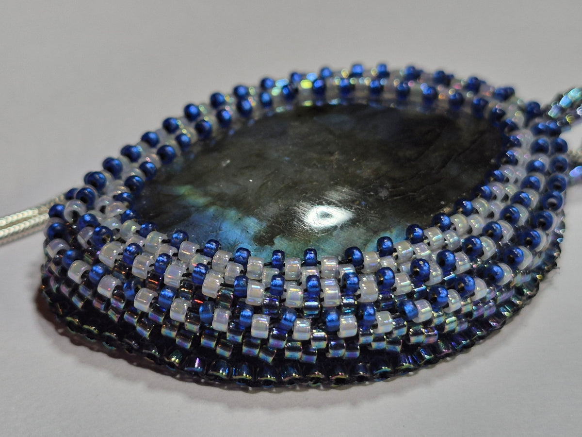 Close-up of blue, white, and iridescent beadwork framing the smoky oval cabochon.