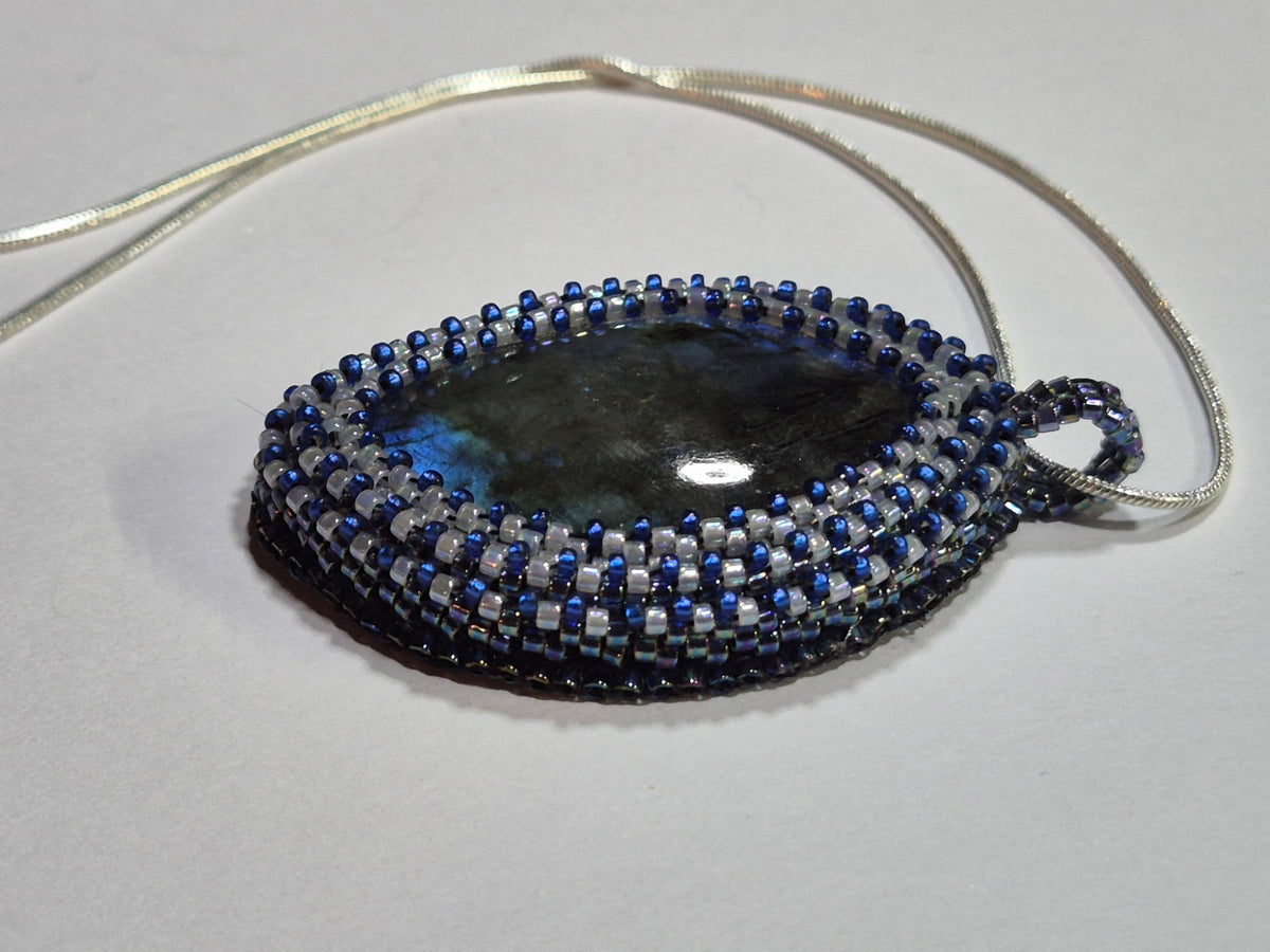Side view of the oval cabochon pendant showing its woven bezel and matching beaded bail.