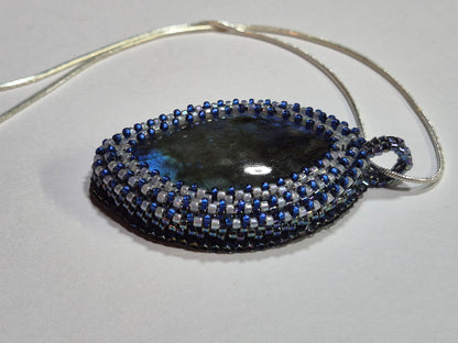 Side view of the oval cabochon pendant showing its woven bezel and matching beaded bail.