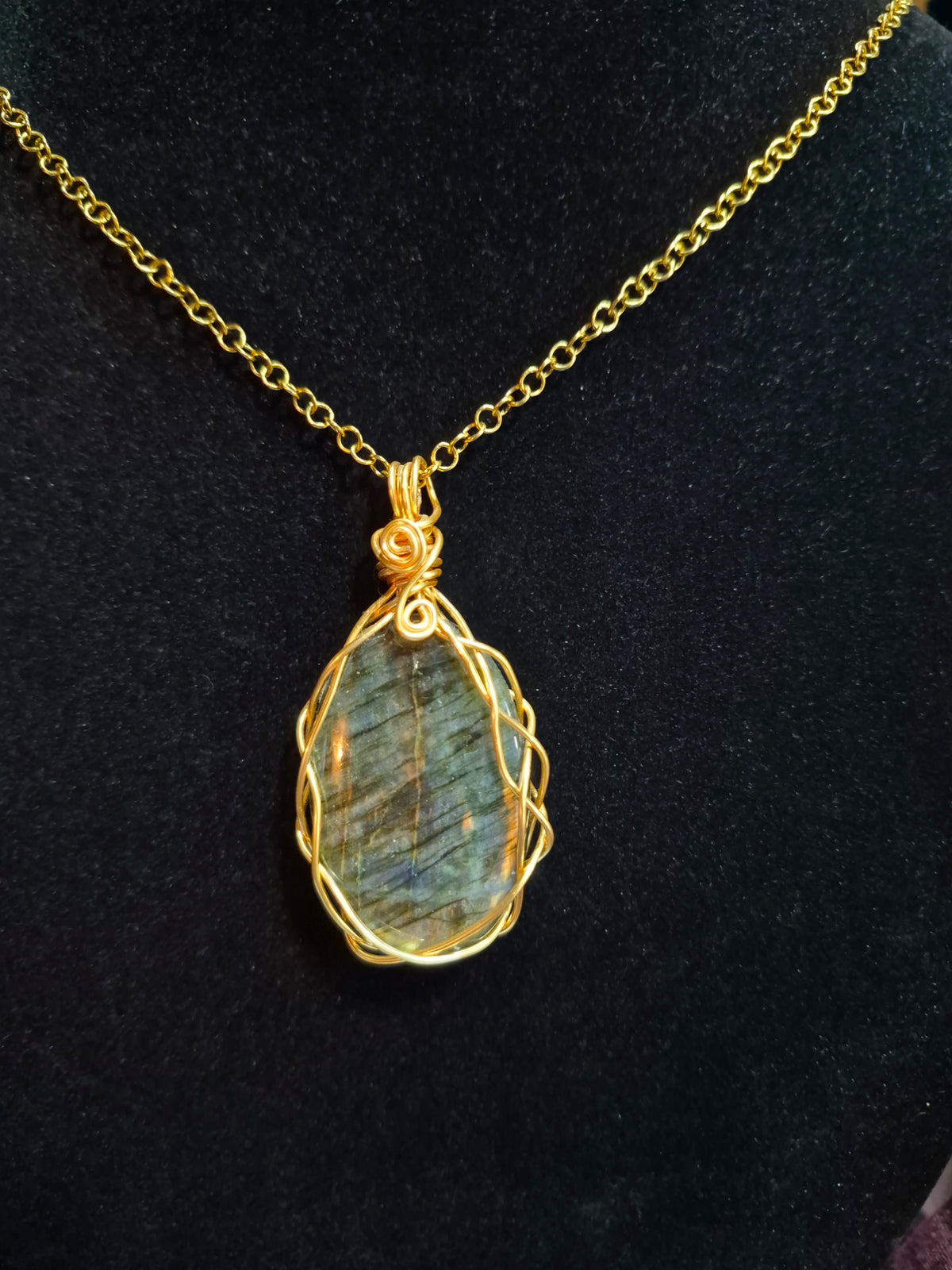 Labradorite pendant in a braided gold-tone copper wire frame hanging on a chain against black.