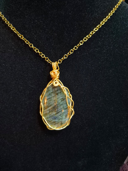 Labradorite pendant in a braided gold-tone copper wire frame hanging on a chain against black.