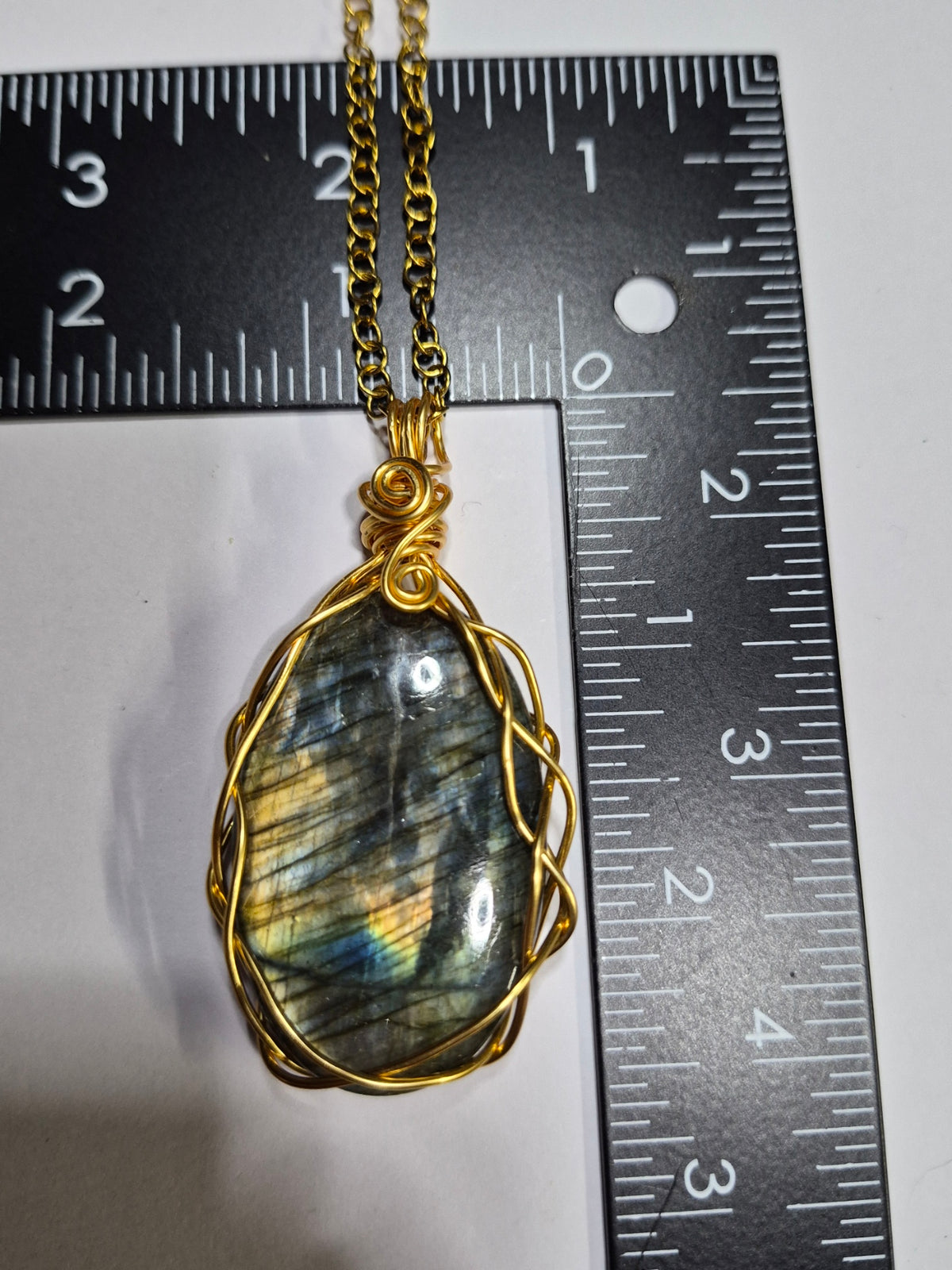 Labradorite pendant with gold-tone braided wirework beside a ruler for scale.