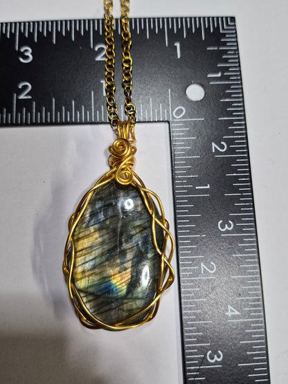 Labradorite pendant with gold-tone braided wirework beside a ruler for scale.