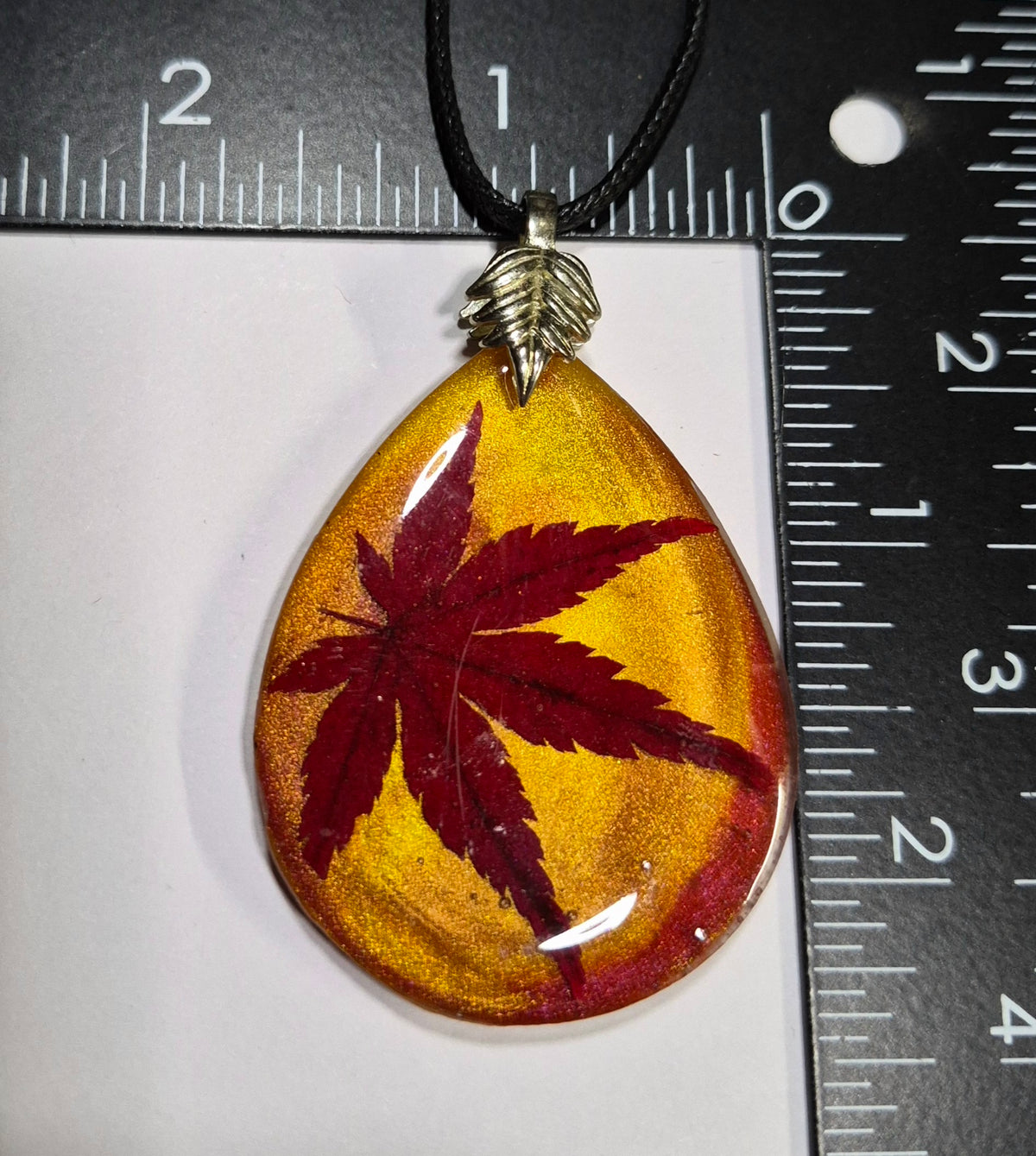 Japanese maple leaf resin teardrop pendant beside a ruler for scale.