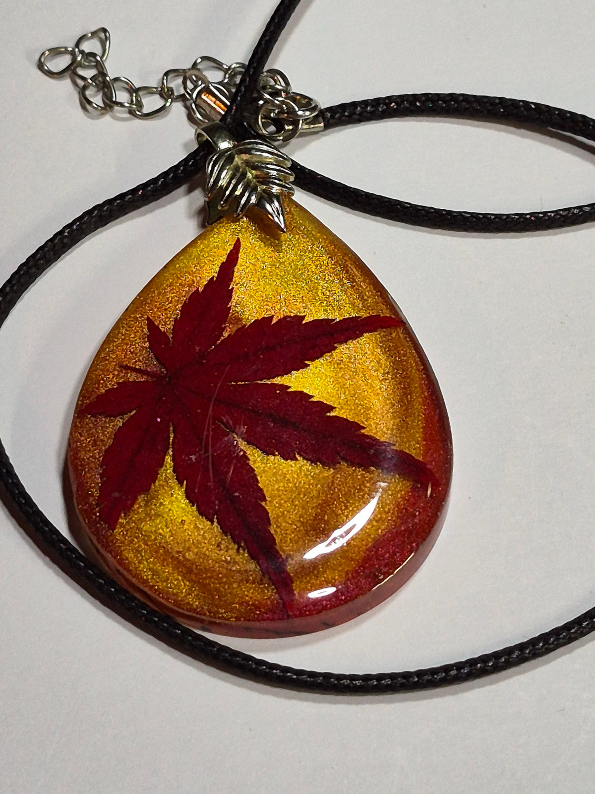 Close-up of a red Japanese maple leaf embedded in gold-shimmer resin with a silver-tone leaf bail.