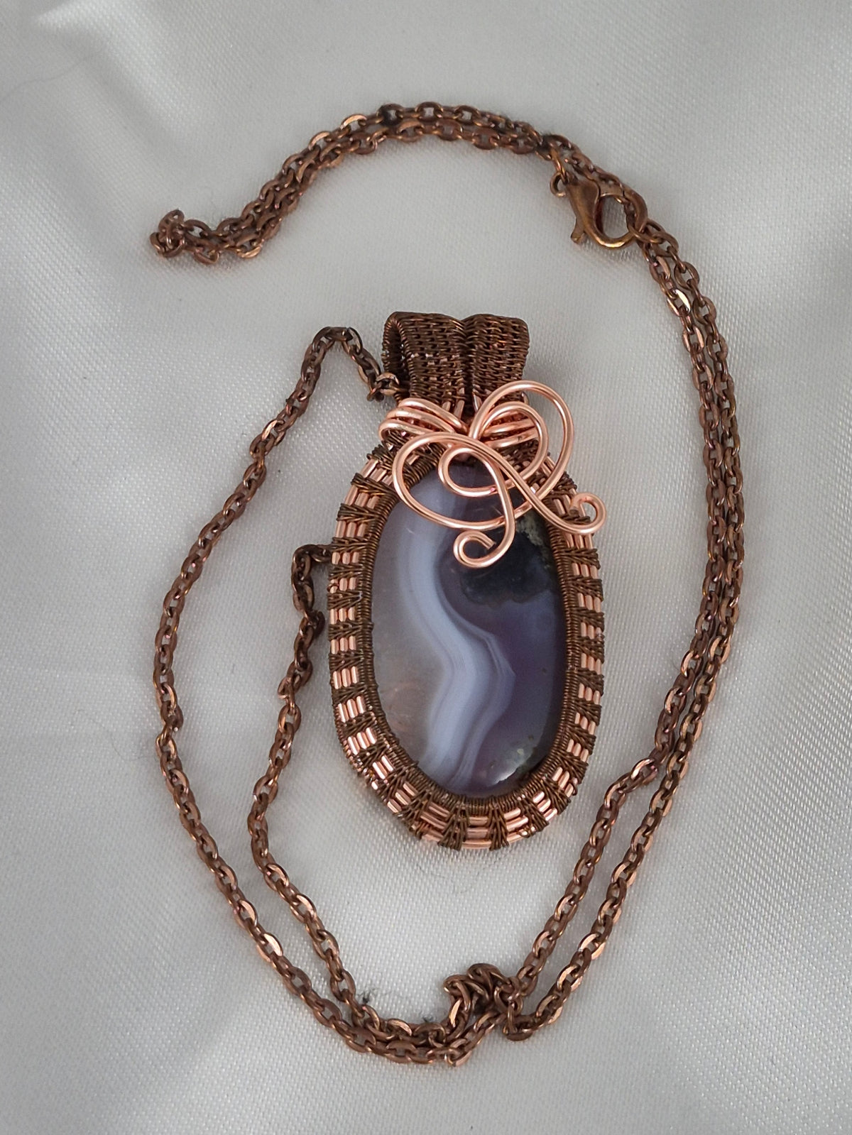 Copper-wrapped oval stone necklace and chain laid out on pale fabric.