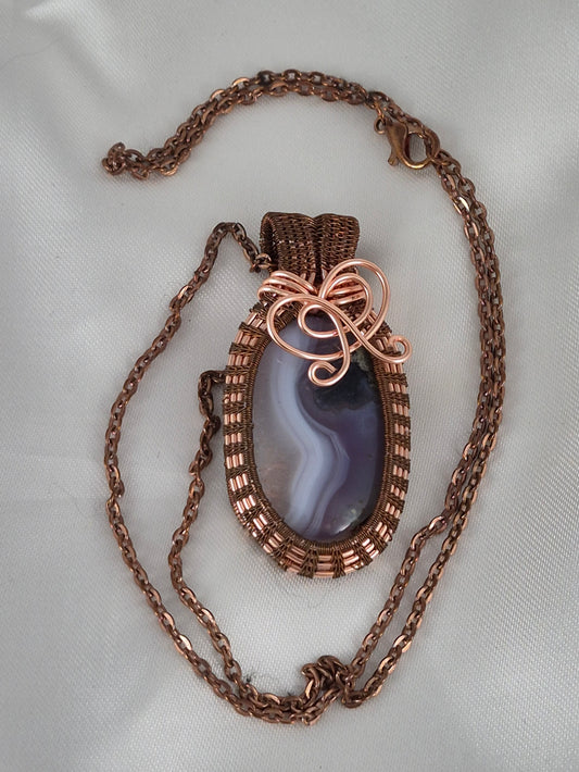 Copper-wrapped oval stone necklace and chain laid out on pale fabric.