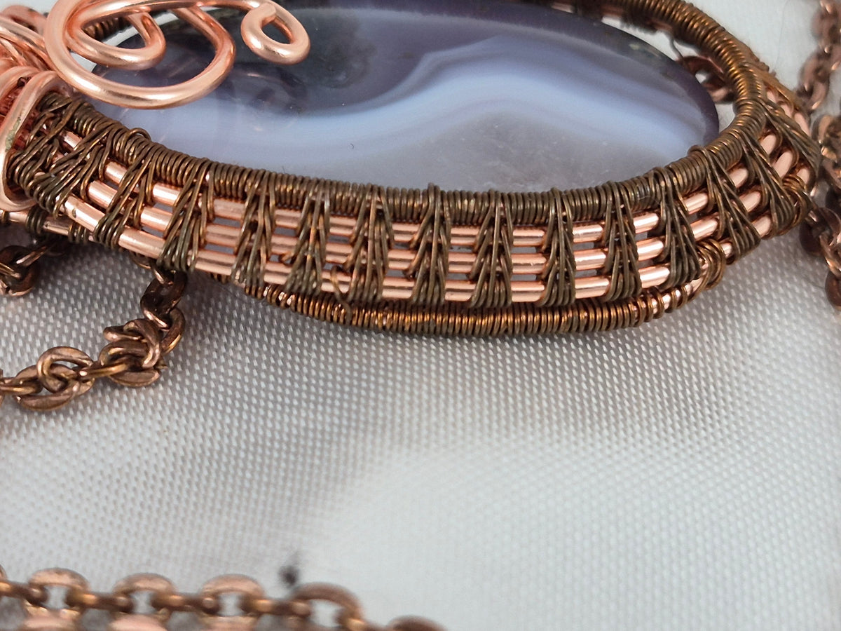 Close-up of the tightly woven copper wire frame around the banded oval stone.