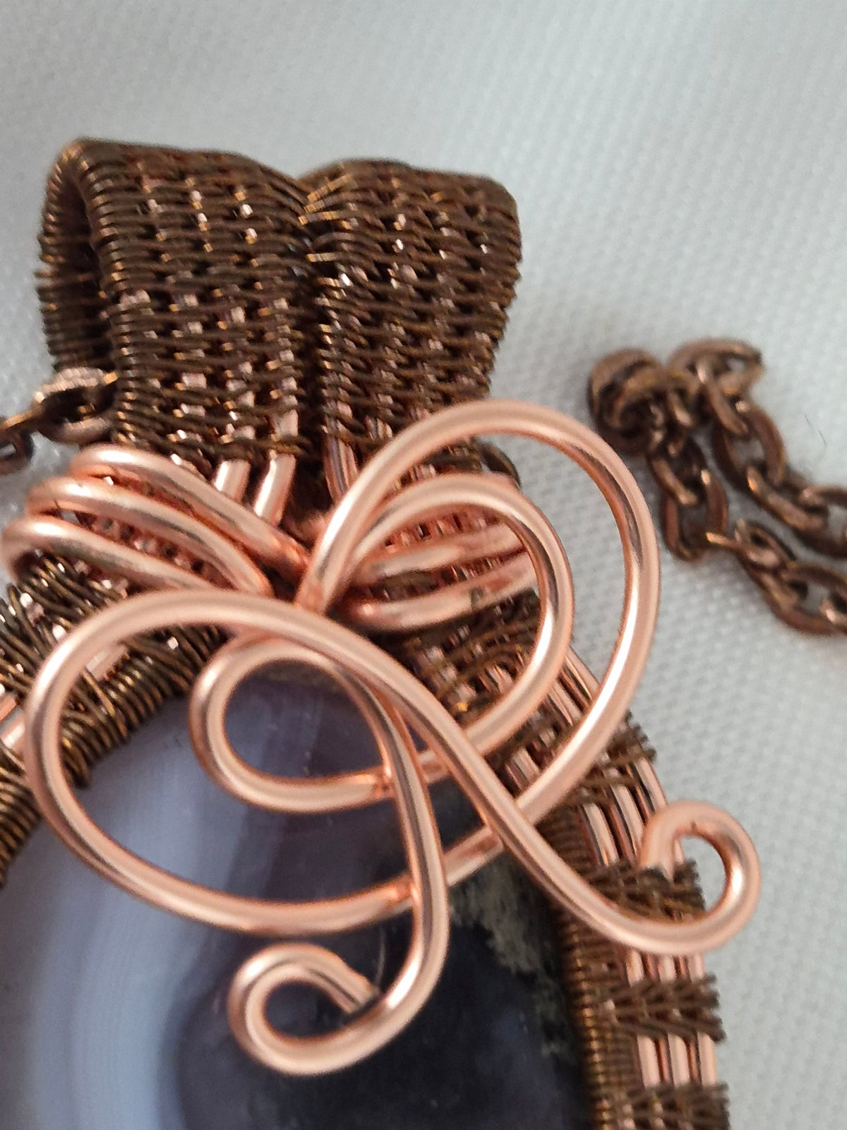 Close-up of the woven copper bail and curved decorative scrollwork.