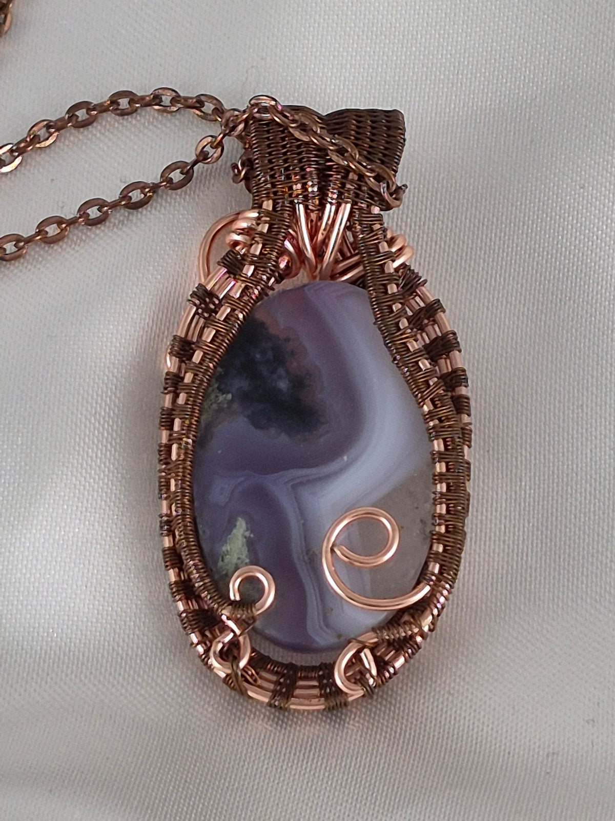 Back view of the banded oval stone pendant showing copper wirework and curled securing accents.