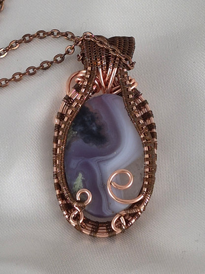 Back view of the banded oval stone pendant showing copper wirework and curled securing accents.