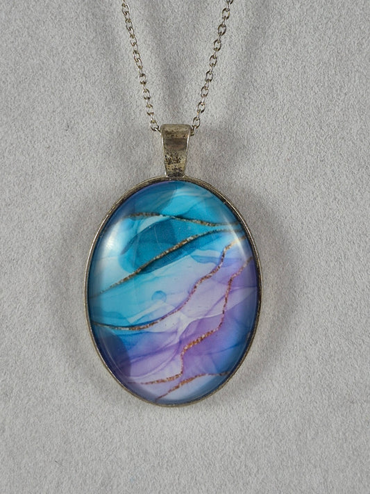 Blue and lavender oval cabochon pendant with gold-toned lines in a silver-tone setting hanging on a chain.