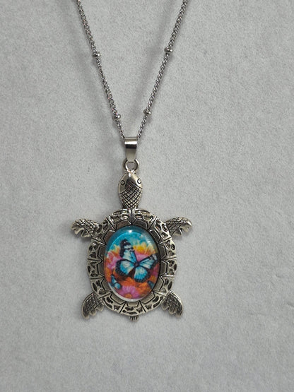 Silver-tone sea turtle pendant with a blue butterfly floral cabochon hanging from a chain.